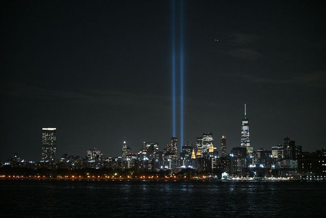The blueish beams of light in the sky from lower manhattan, with the World Trade Center and other buildings in Manhattan, as seen at night